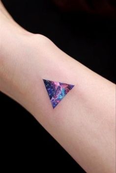 a small triangle tattoo on the right arm with galaxy and stars in space behind it