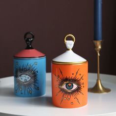 three ceramic containers with designs on them sitting on a table next to a candle holder