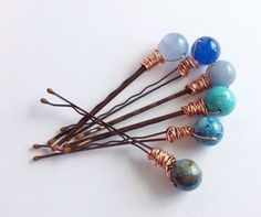 four different colored beads are on top of some brown hair pins with wire wrapped around them