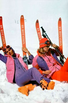 two women sitting in the snow with their skis on