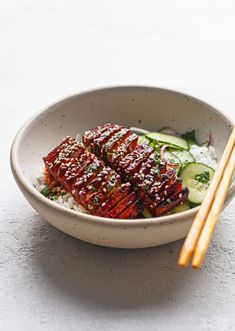 a bowl filled with meat and rice next to chopsticks on a table top