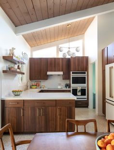 a kitchen with wooden cabinets and white counter tops next to a dining room table filled with oranges