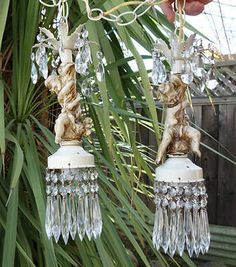 a pair of angel figurines hanging from a chandelier in front of a palm tree