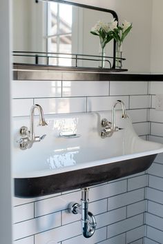 a bathroom sink sitting under a mirror next to a white tiled wall with black trim