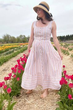 a woman standing in a field full of flowers wearing a dress and hat with her hands on her hips