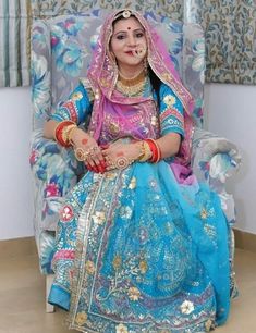 a woman sitting on top of a chair in a blue and pink wedding dress with gold jewelry