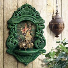 an ornate green frame hangs on the wall next to a potted plant and lamp