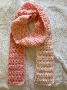 a pink and white knitted scarf laying on top of a bed next to a pillow