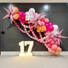 the balloon arch is decorated with pink, white and orange balloons that spell out 17