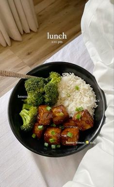 a black bowl filled with rice, broccoli and tofu on top of a table