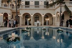 a wedding party in front of a large building next to a pool with candles on it