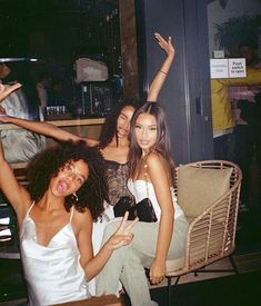 three young women posing for the camera with their arms in the air while sitting on a chair