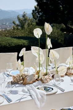 the table is set with white flowers and place settings