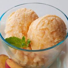 two scoops of ice cream in a glass bowl with peaches on the side