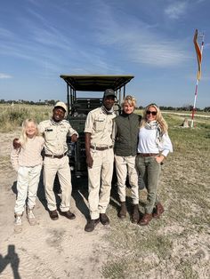 a group of people standing next to each other in front of a vehicle on a dirt road