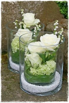 three clear vases filled with white flowers and greenery sitting on a stone surface