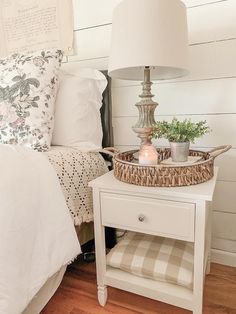 a white nightstand with a basket on it next to a bed