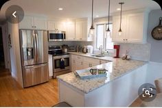 a kitchen with stainless steel appliances and marble counter tops, along with white cabinets and wood floors