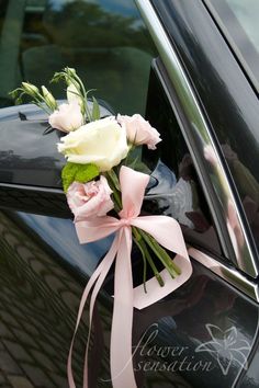 a bouquet of white and pink roses is tied to the side of a car door