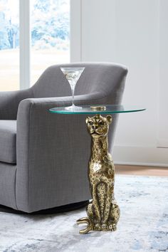 a glass table with a gold cat sitting on top of it next to a gray chair