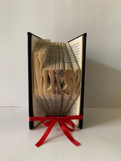 an open book with the word love cut out of it and red ribbon tied around it