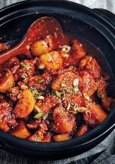 a close up of a stew in a crock pot with a wooden spoon on the side