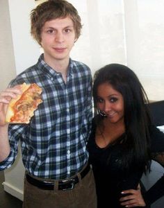 a man and woman standing next to each other in front of a window holding pizza