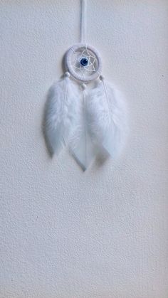 a white feather dream catcher hanging on a wall with an evil eye in the center