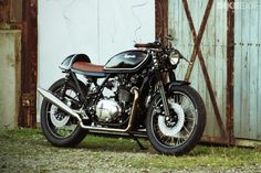 a black motorcycle parked in front of a wooden building with an old door behind it