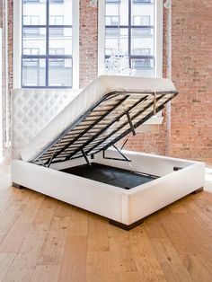 a bed frame with a mattress underneath it in front of a window and brick wall