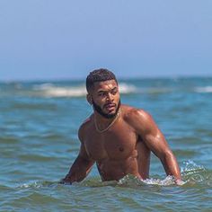 a man standing in the ocean with his shirt off and no shirt on, looking at the camera