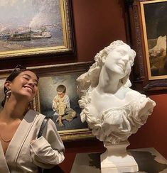 a woman standing next to a busturine in front of paintings on the wall