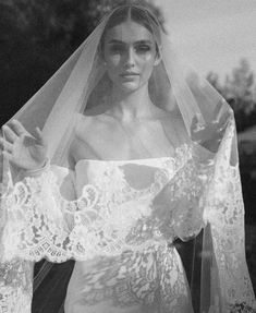 black and white photograph of a woman in wedding dress with veil over her head looking at the camera