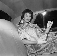 a woman sitting in the back seat of a car holding her hand up and waving