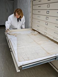 a woman in a white lab coat is looking at some drawers