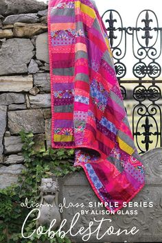 a pink and yellow blanket sitting on top of a stone wall