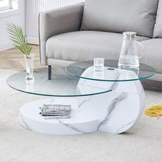 a marble coffee table with glass top in front of a gray couch and white rug