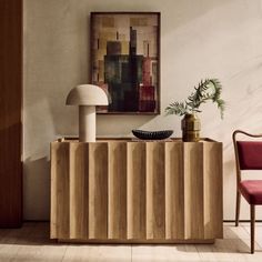 a wooden cabinet sitting next to a table with a lamp on it and a chair