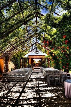 an outdoor venue set up with tables and chairs under a canopy covered in greenery