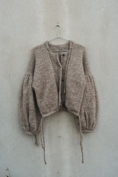 an old sweater hanging on a clothes hanger against a white wall with no one in it