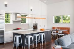 a kitchen and living room with white cabinets, wood flooring and bar stools