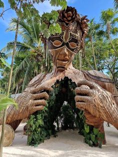 a statue made out of wood and plants in front of palm trees on the beach