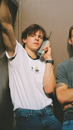 two young men sitting next to each other while talking on their cell phones and one holding a phone up to his ear