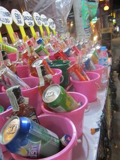 pink buckets filled with various types of drinks on a white tablecloth covered street