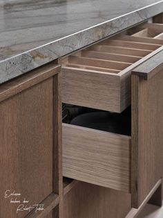 an open drawer in the middle of a kitchen counter with marble top and wooden drawers