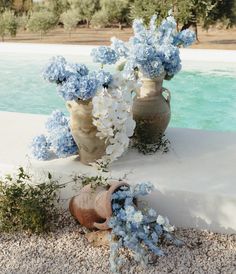 two vases filled with blue and white flowers on top of gravel near a pool