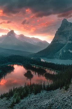 the sun is setting over a mountain lake with trees and mountains in the back ground