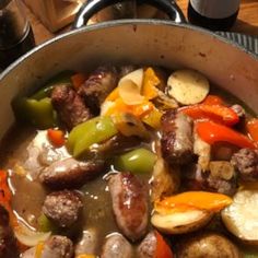 a pan filled with meat and vegetables on top of a wooden table next to a glass of beer