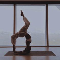 a person doing a handstand on a yoga mat in front of large windows