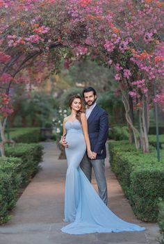 a pregnant couple standing under an archway with pink flowers on the trees in front of them